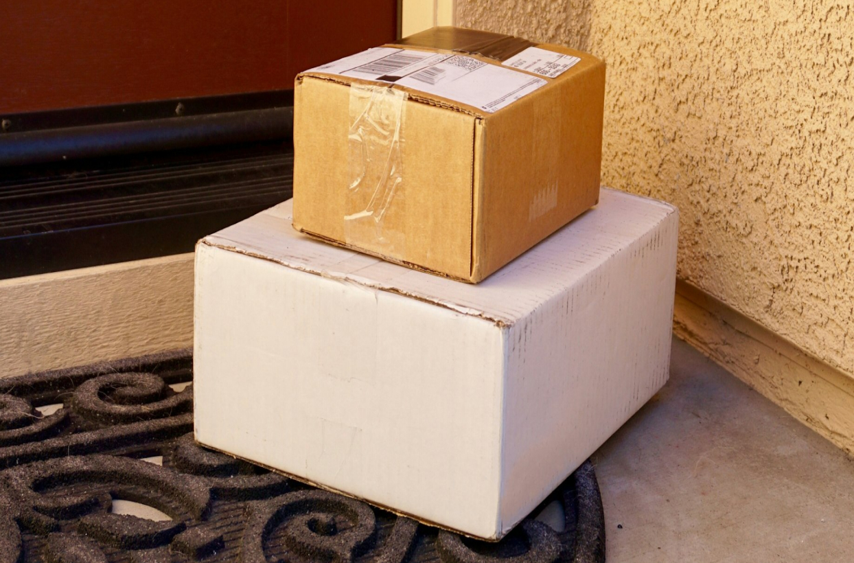 Two sealed packages stacked on a decorative mat in front of a brown door.
