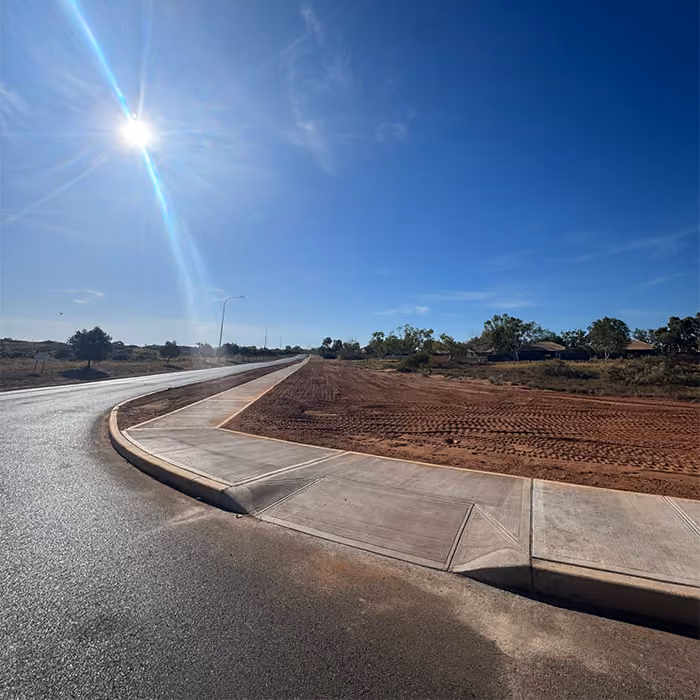 Two dump trucks and a road roller paving asphalt on a remote highway near dry hills and railway tracks.