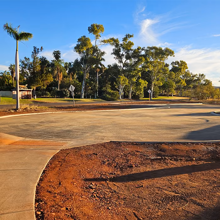 Two dump trucks and a road roller paving asphalt on a remote highway near dry hills and railway tracks.