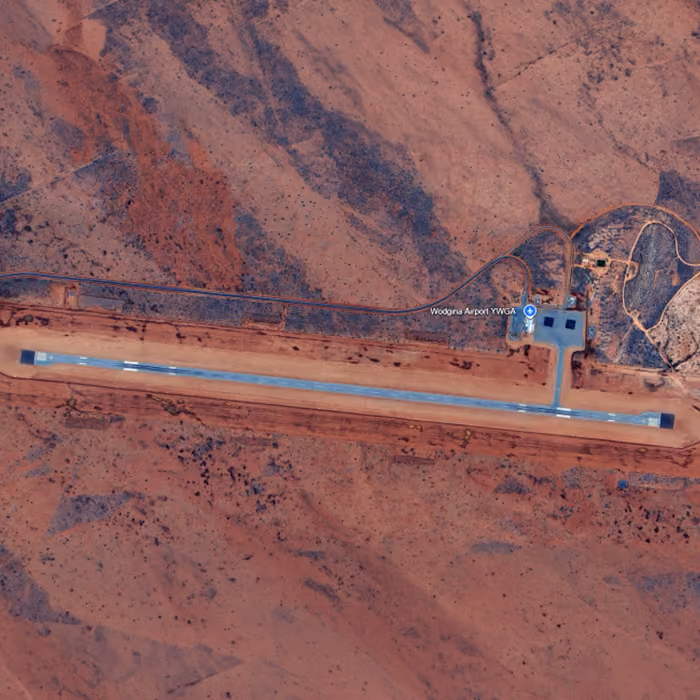 Two dump trucks and a road roller paving asphalt on a remote highway near dry hills and railway tracks.