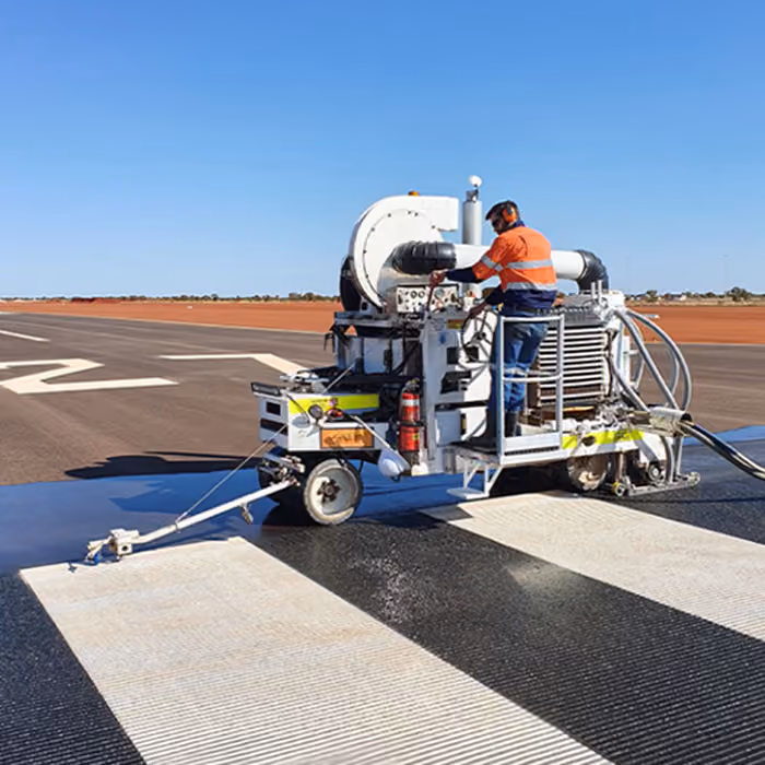 Two dump trucks and a road roller paving asphalt on a remote highway near dry hills and railway tracks.