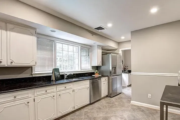 Bright kitchen with white cabinets, black countertop, stainless steel appliances, and a large window.