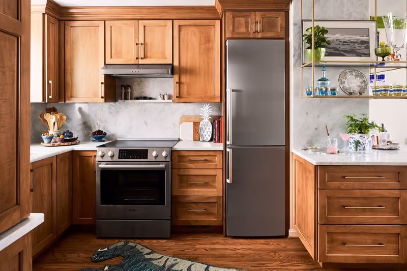 Modern kitchen with wooden cabinets, stainless steel oven, fridge, marble countertops, and floor rug.