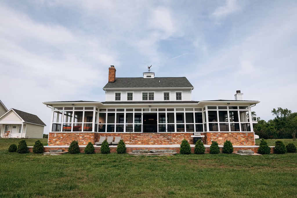 Large two-story white house with screened porch, red brick foundation, and green lawn in front.