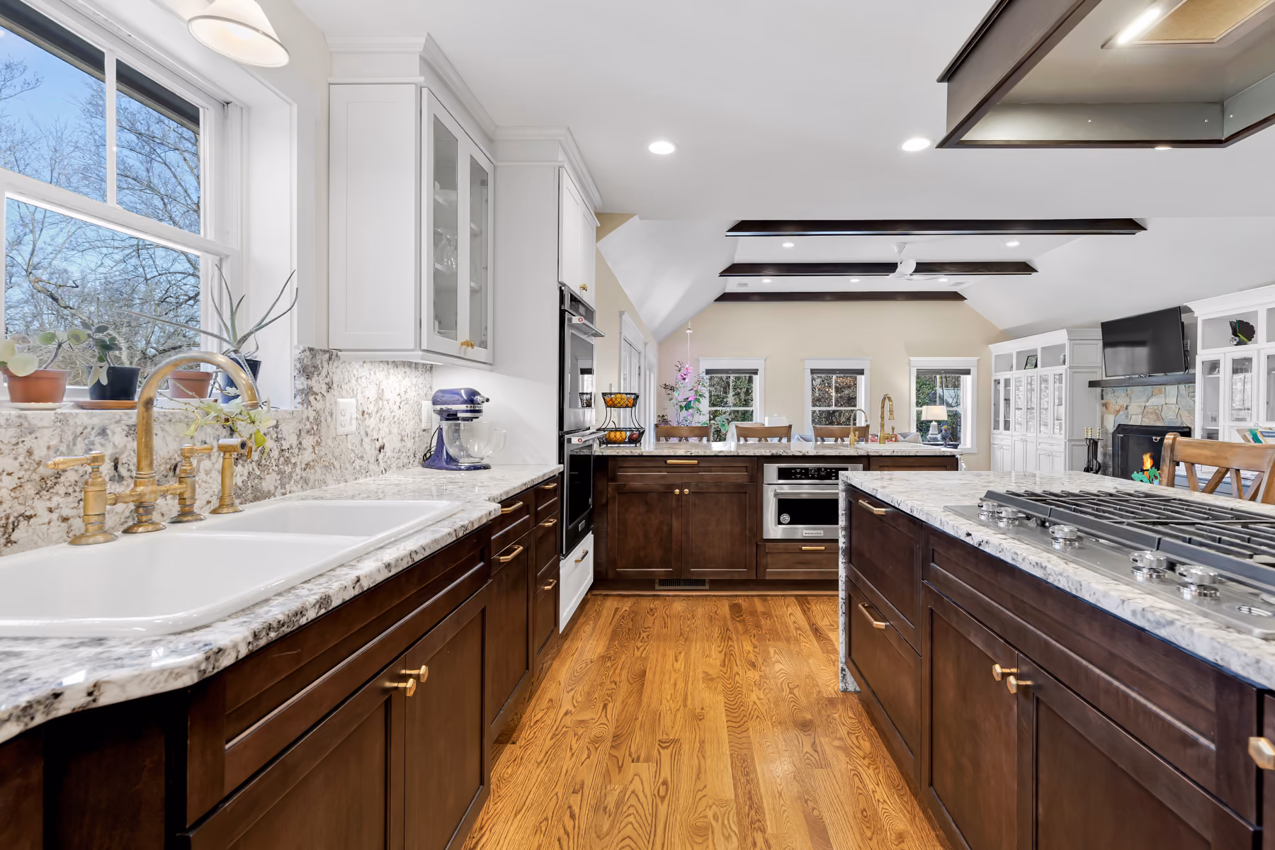 Modern kitchen with dark wood cabinets, marble countertops, double sinks, and a gas stove on an island.
