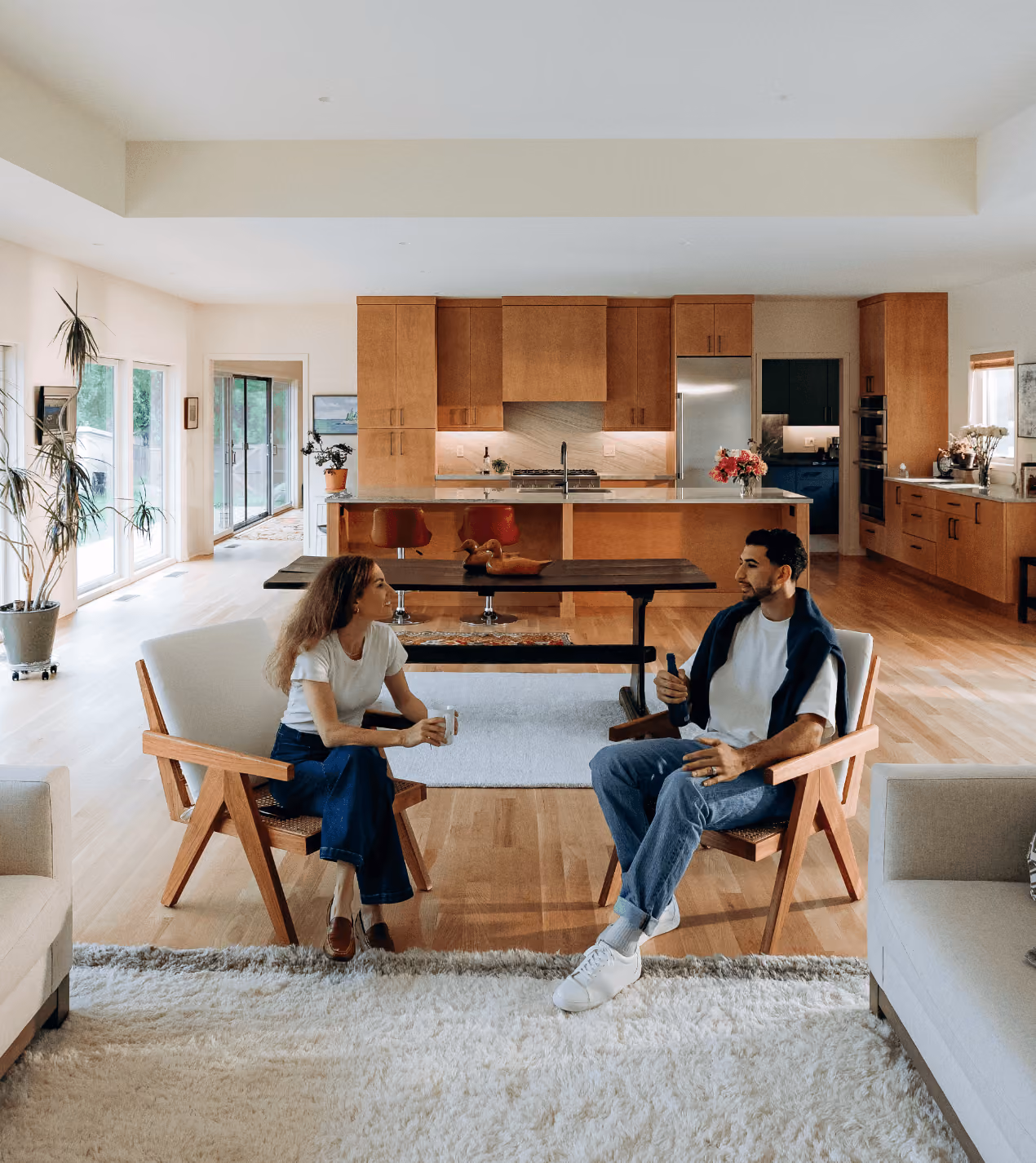 Man and woman sitting in wooden chairs facing each other in a spacious kitchen and living area.