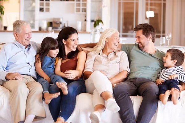 Happy three-generation family sitting on a couch, smiling and enjoying time together indoors.