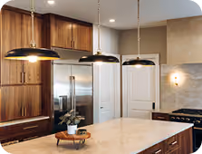Modern kitchen with wooden cabinets, marble island, three black pendant lights, and stainless steel appliances.