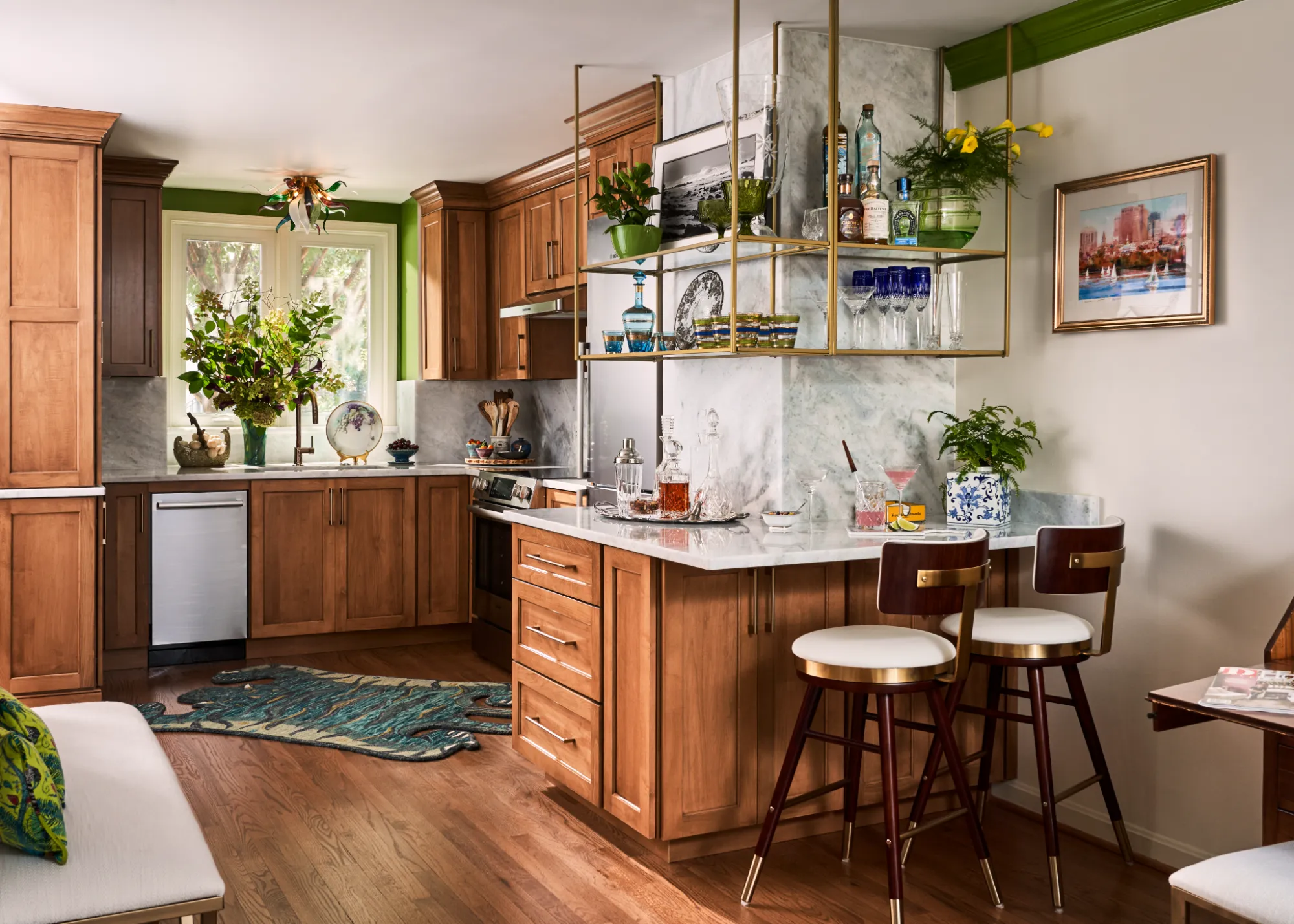 Warm wooden kitchen with marble countertops, green accents, hanging shelves with glassware, and bar stools.