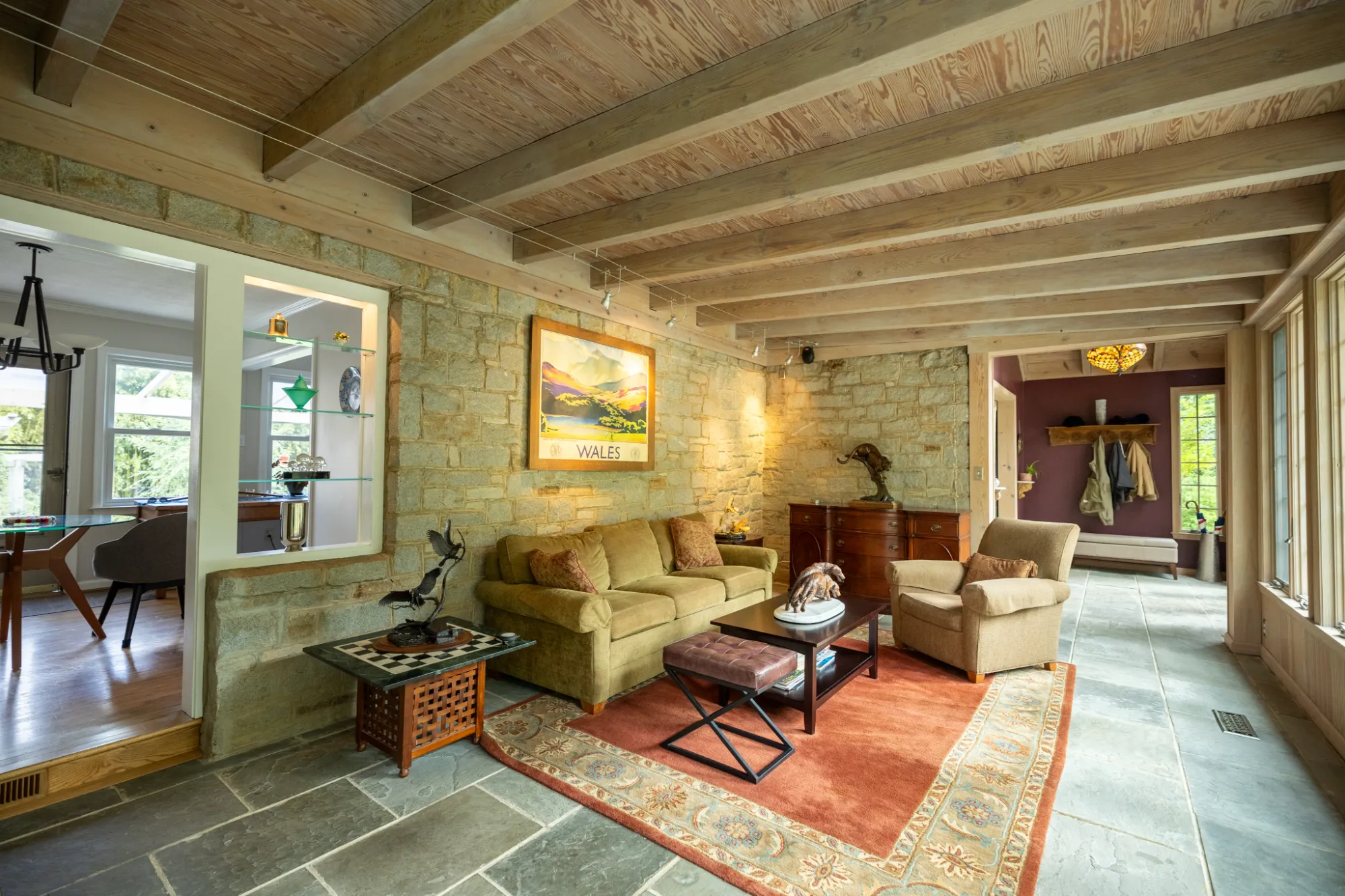 Cozy living room with stone walls, wooden ceiling beams, sofa, armchair, and large windows.