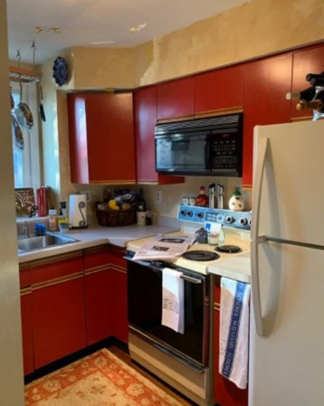 Compact kitchen with red cabinets, white countertops, stove, microwave, and a refrigerator.