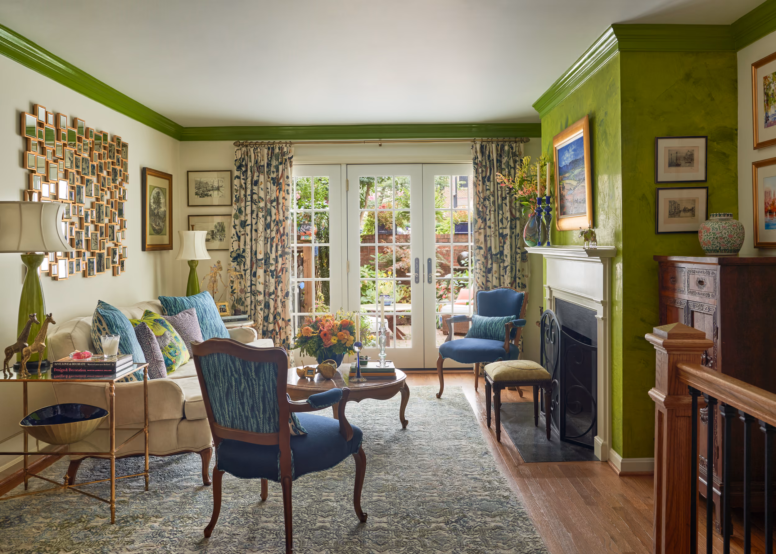 Living room with blue armchairs, floral curtains, green trim, and glass doors opening to a garden patio.
