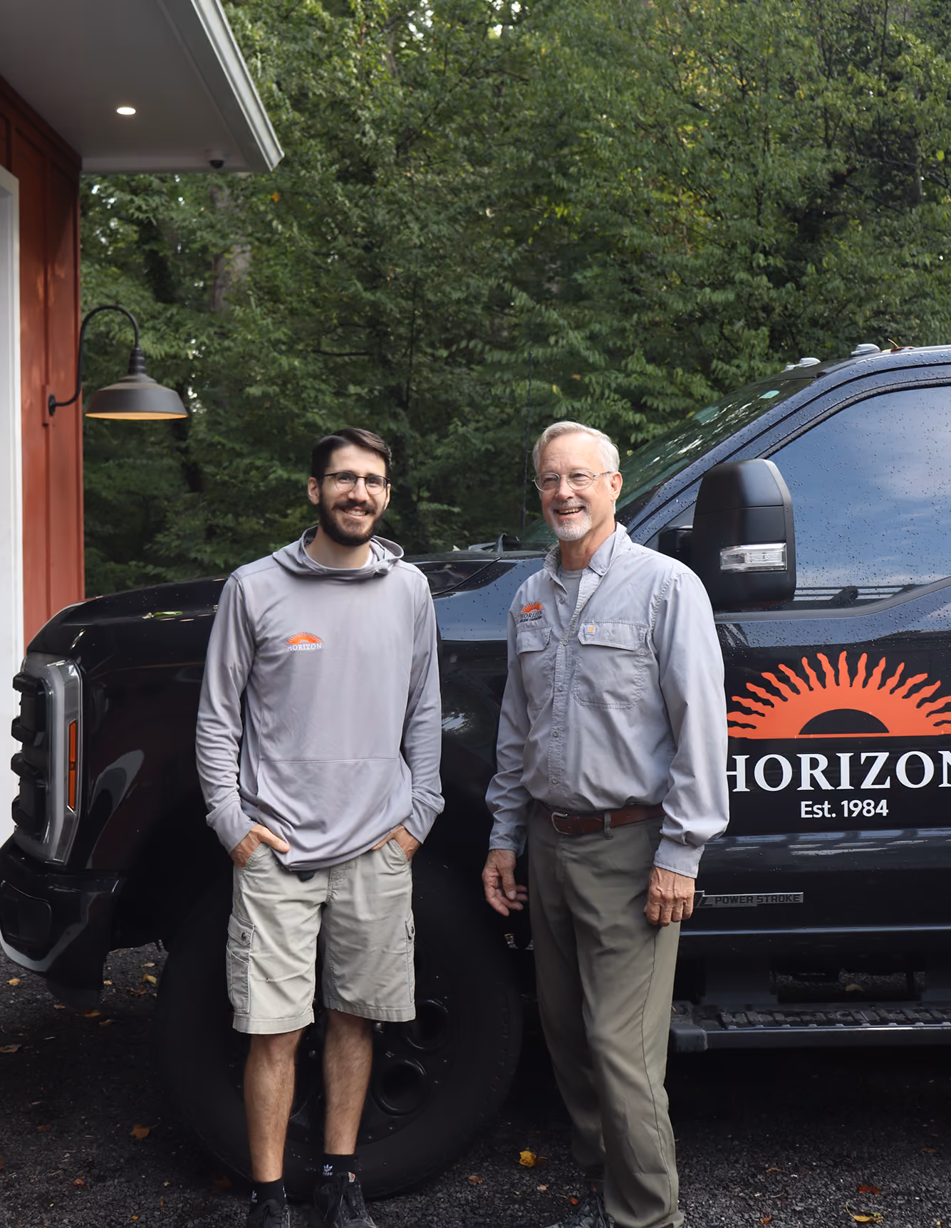 Two men smiling, standing by a black truck with Horizon logo and Est. 1984 text.