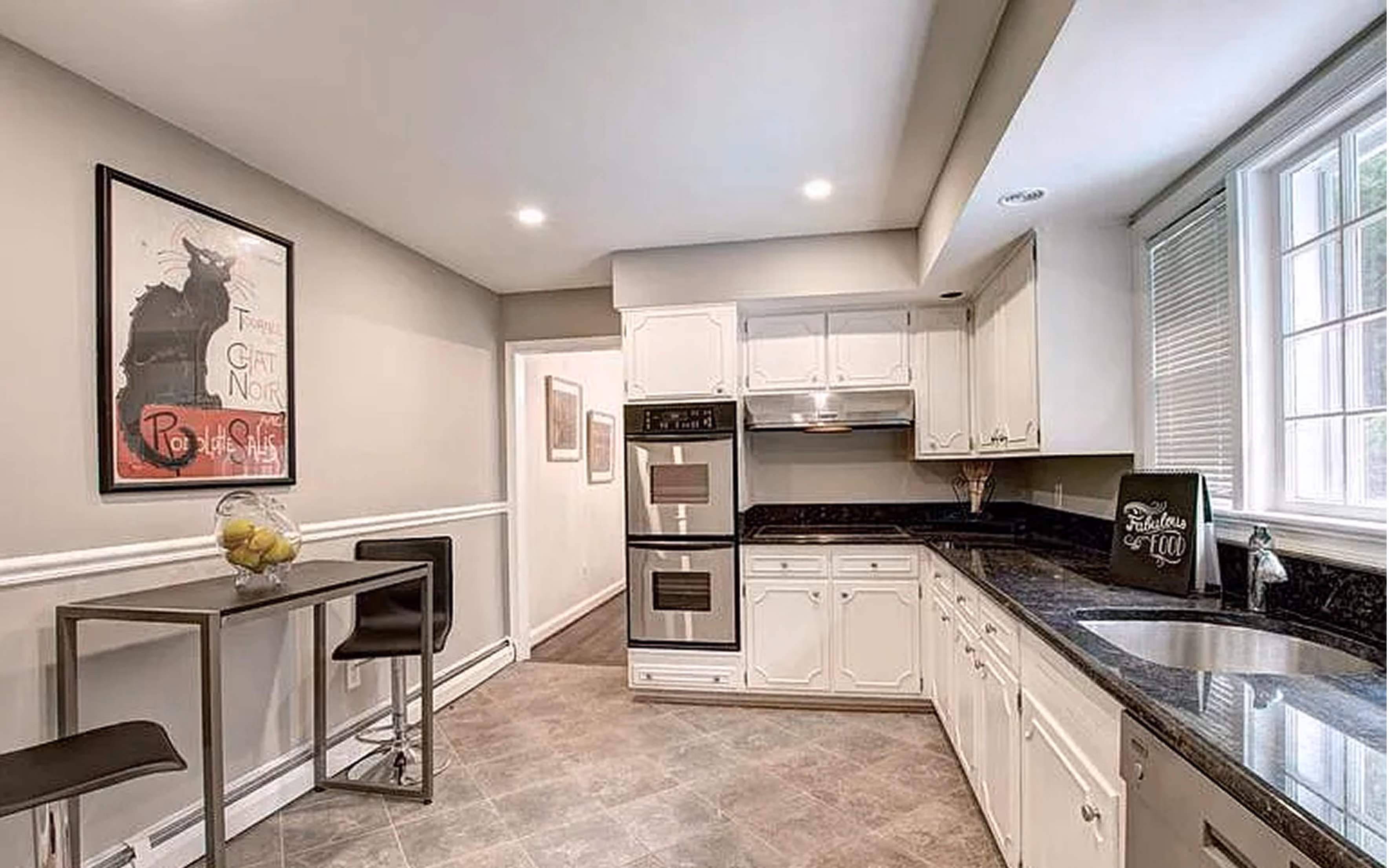 Modern kitchen with white cabinets, black granite counters, double oven, and bar table with stools.