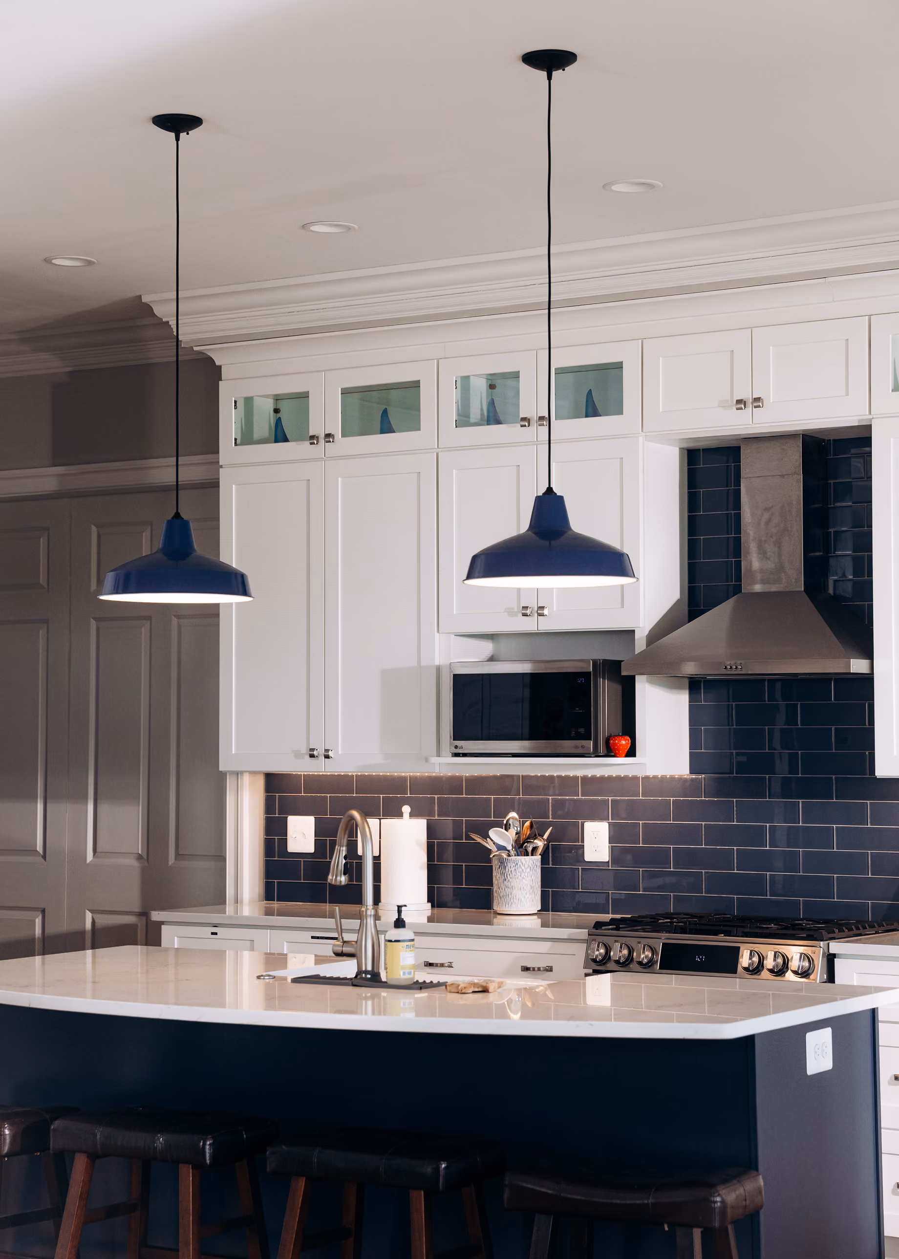 Modern kitchen with white cabinets, dark blue tile backsplash, blue pendant lights, and a large island with stools.