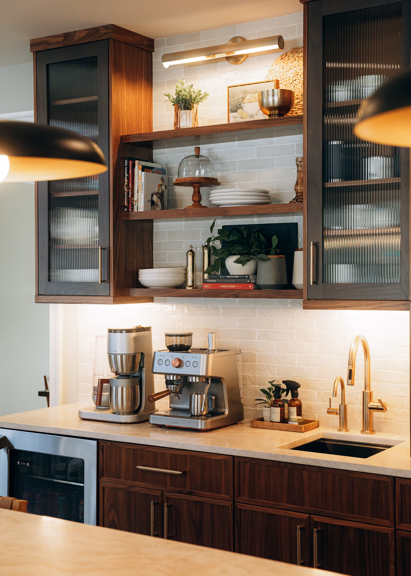 Modern kitchen countertop with coffee makers, gold faucet, plants, and wooden cabinets with glass doors.