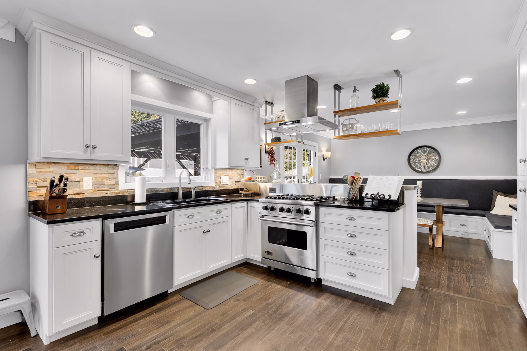 Modern kitchen with white cabinets, stainless steel stove and dishwasher, granite counters, and wooden floor.