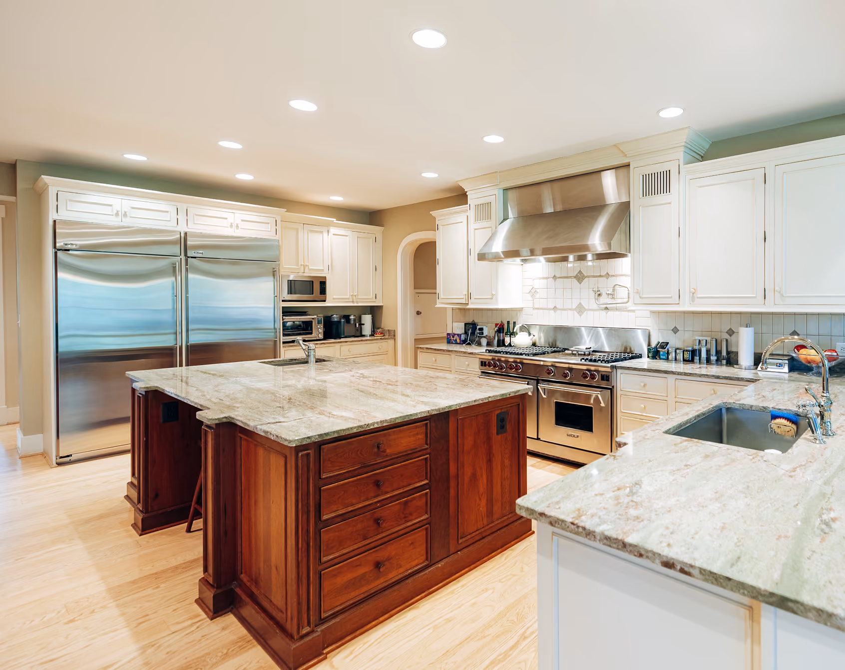 Modern kitchen with marble countertops, wooden island, white cabinets, stainless steel appliances, and hardwood floor.
