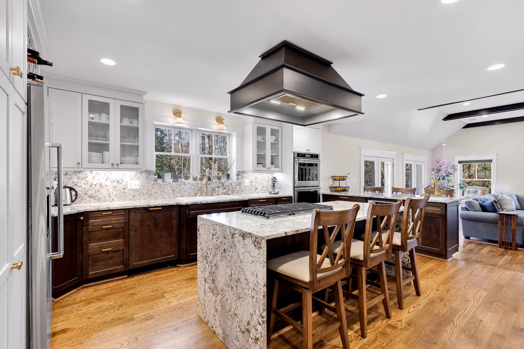 Modern kitchen with marble island, wooden stools, white and dark cabinets, and hardwood floors.