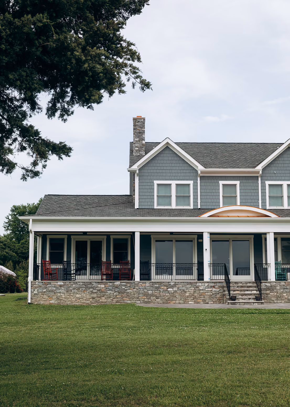 Large two-story house with gray siding, stone foundation, porch, and green lawn in front.