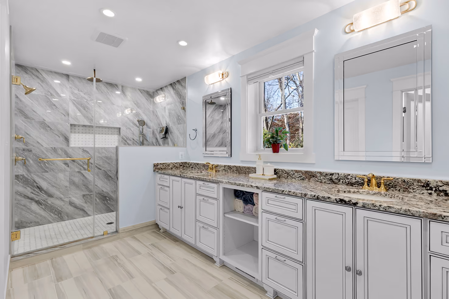 Modern bathroom with double sink granite countertop, white cabinets, and glass enclosed marble shower.