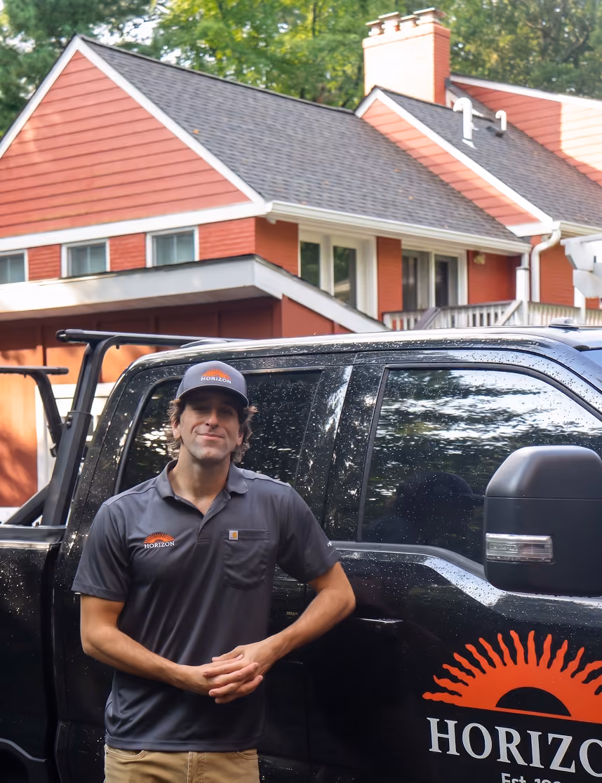 Man in Horizon uniform standing next to black truck with Horizon logo in front of a red house.