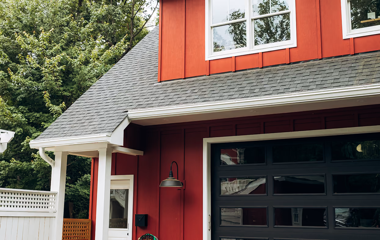 Red house exterior with gray shingled roof, white window frames, and black garage door.