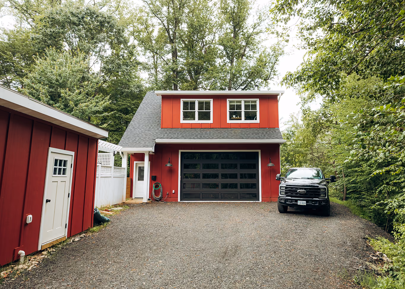 Red detached garage ADU with a black glass garage door set among wooded surroundings