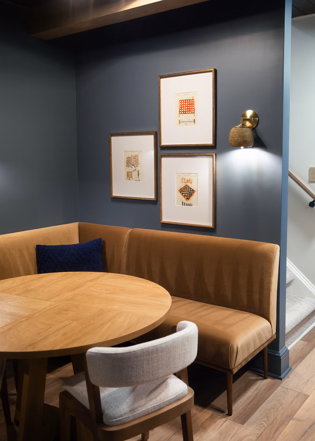 Basement banquette dining nook with a round wood table and navy paneled walls