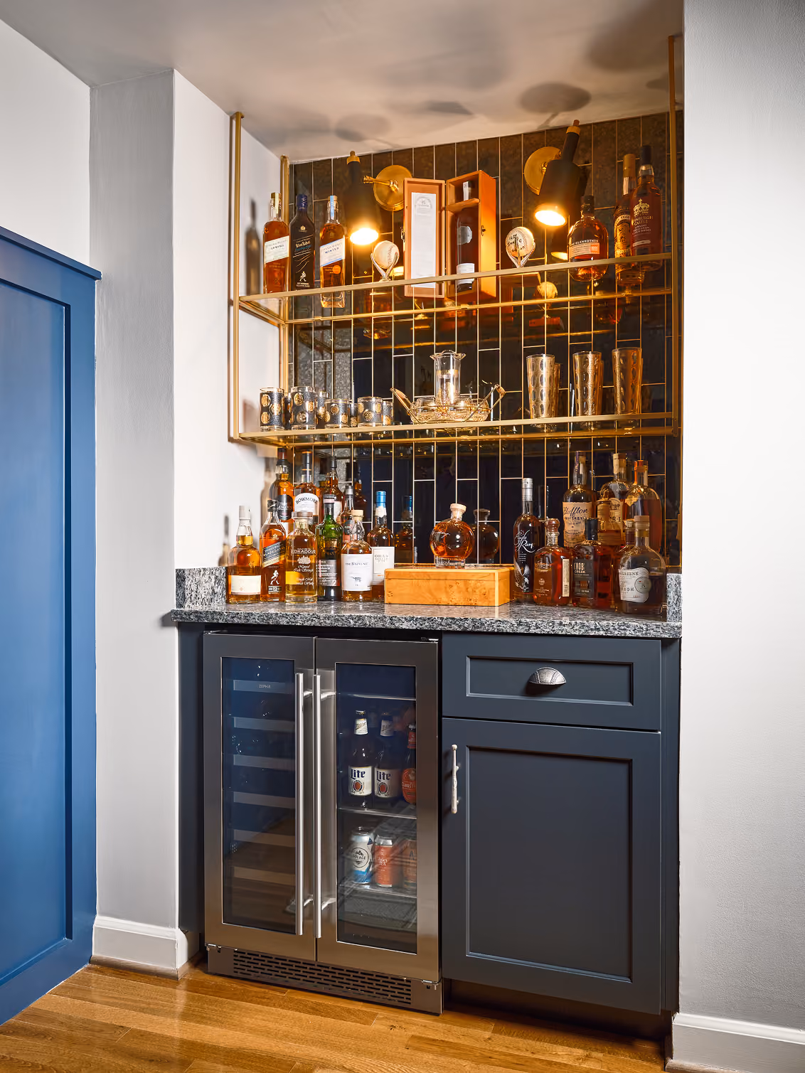 Basement wet bar with navy cabinetry, a wine fridge and lit glass shelving