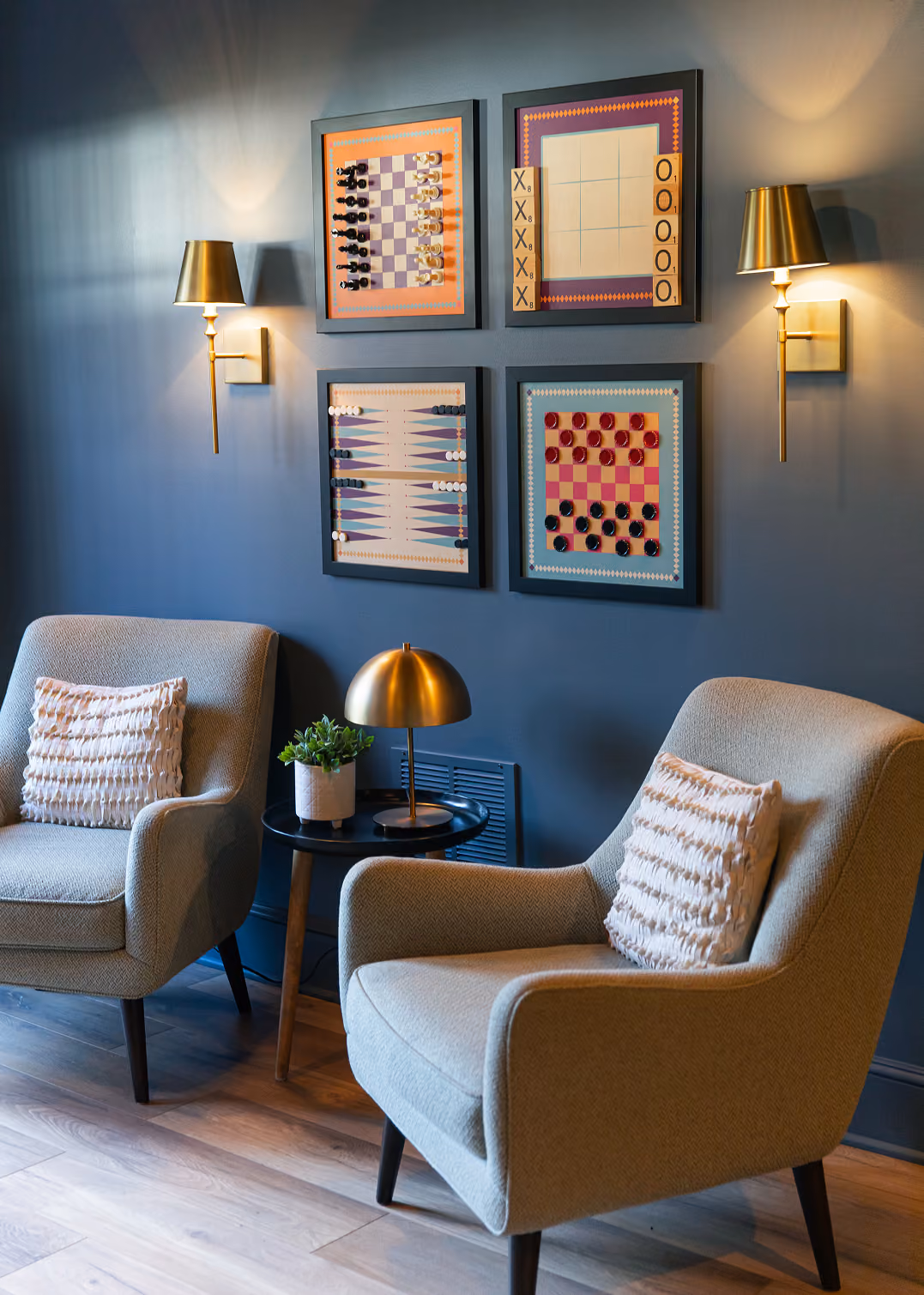 Finished basement sitting nook with two armchairs, brass sconces and framed art on a navy wall