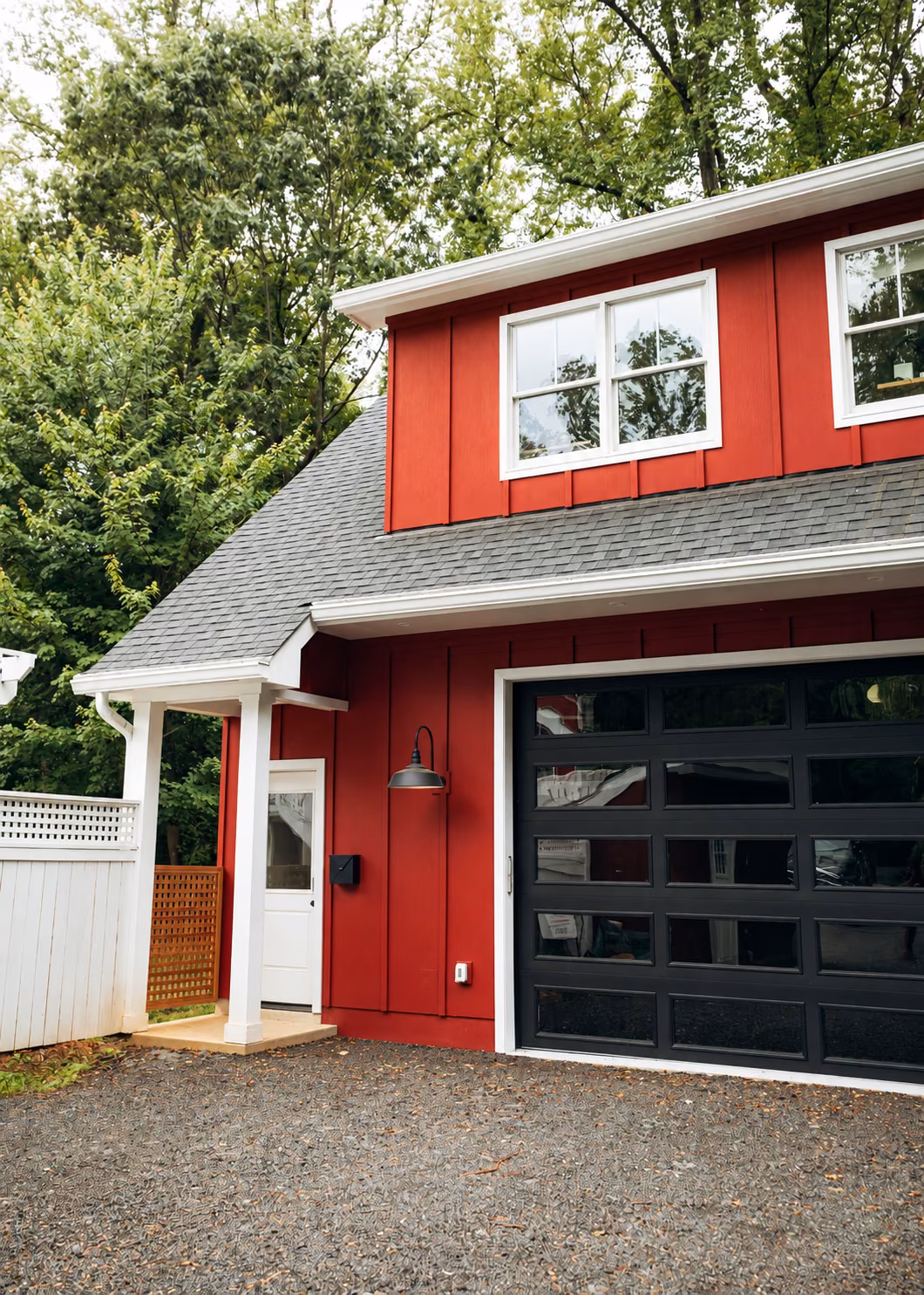 Red board-and-batten garage ADU with a black glass garage door and a second-floor living space