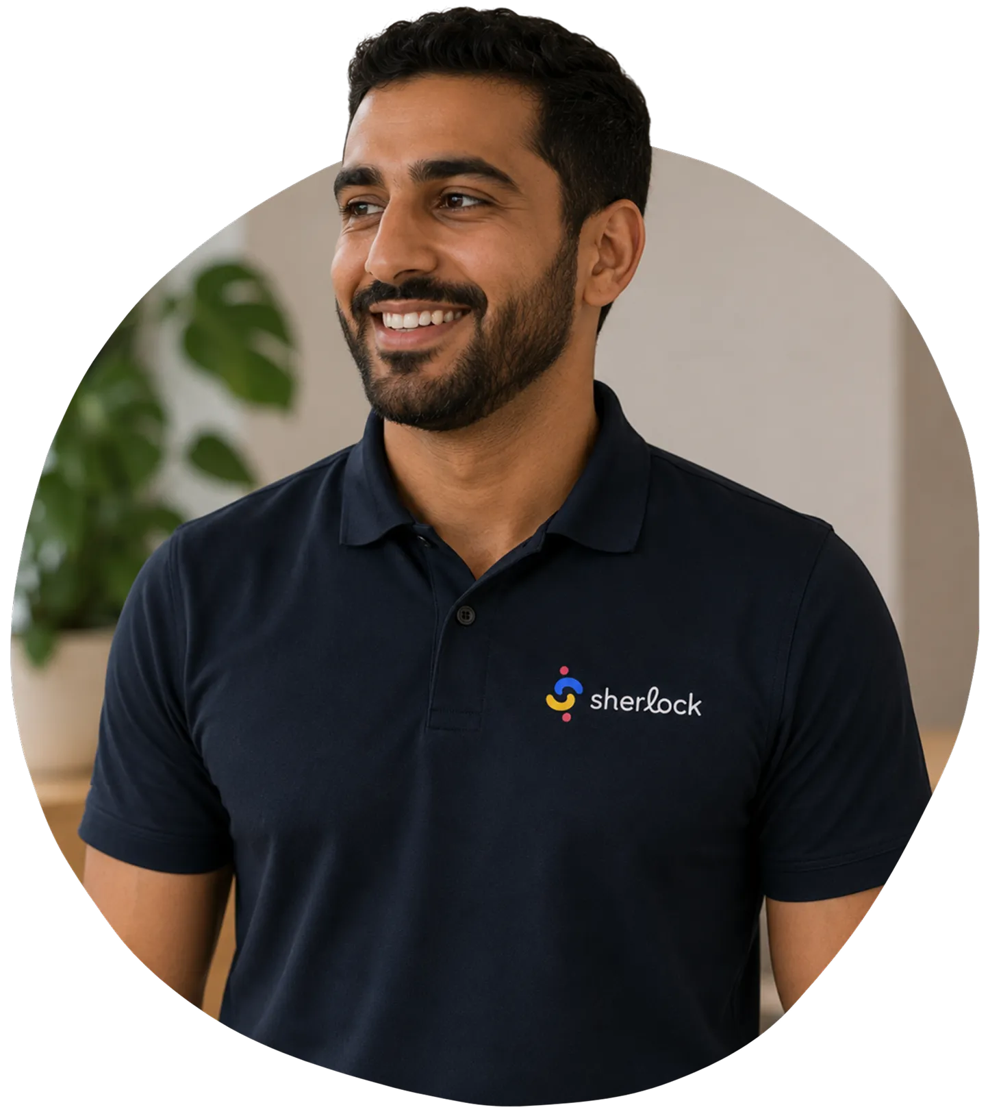 Smiling man wearing a black Sherlock polo shirt with plant in the blurred background.