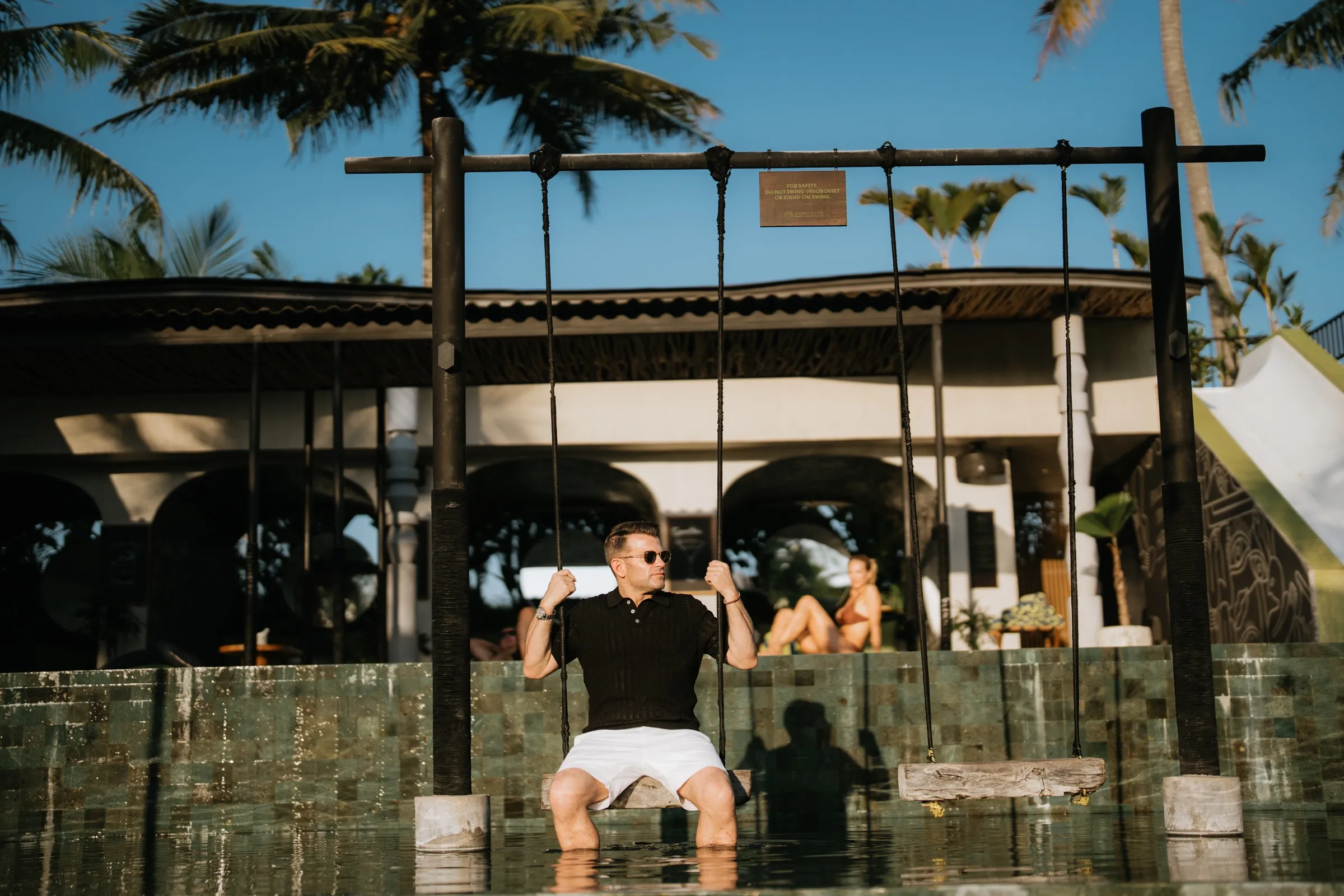 Justin Keeperman seated on a swing at a tropical resort