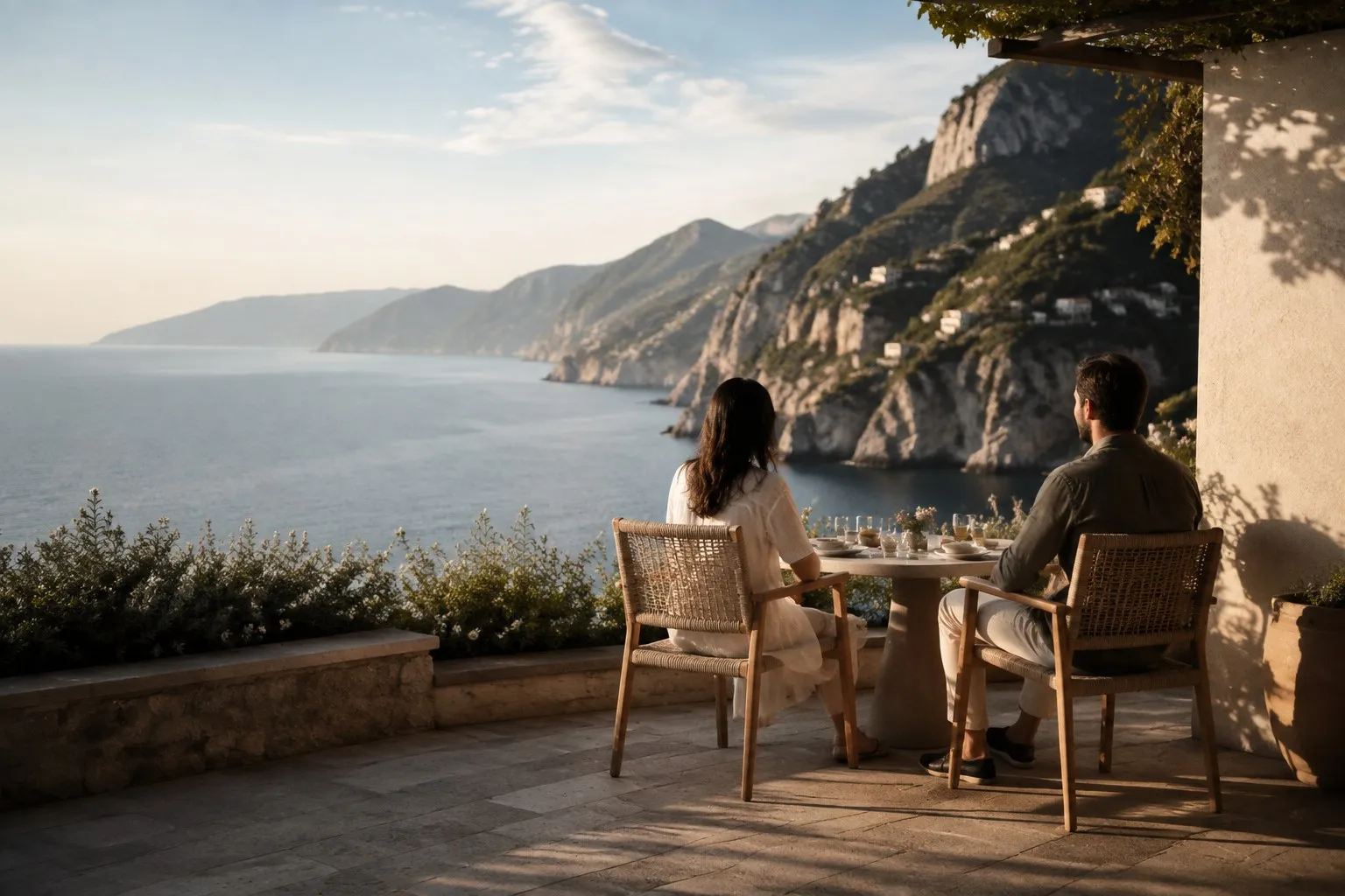 A couple at a terrace table above the Amalfi coastline at golden hour