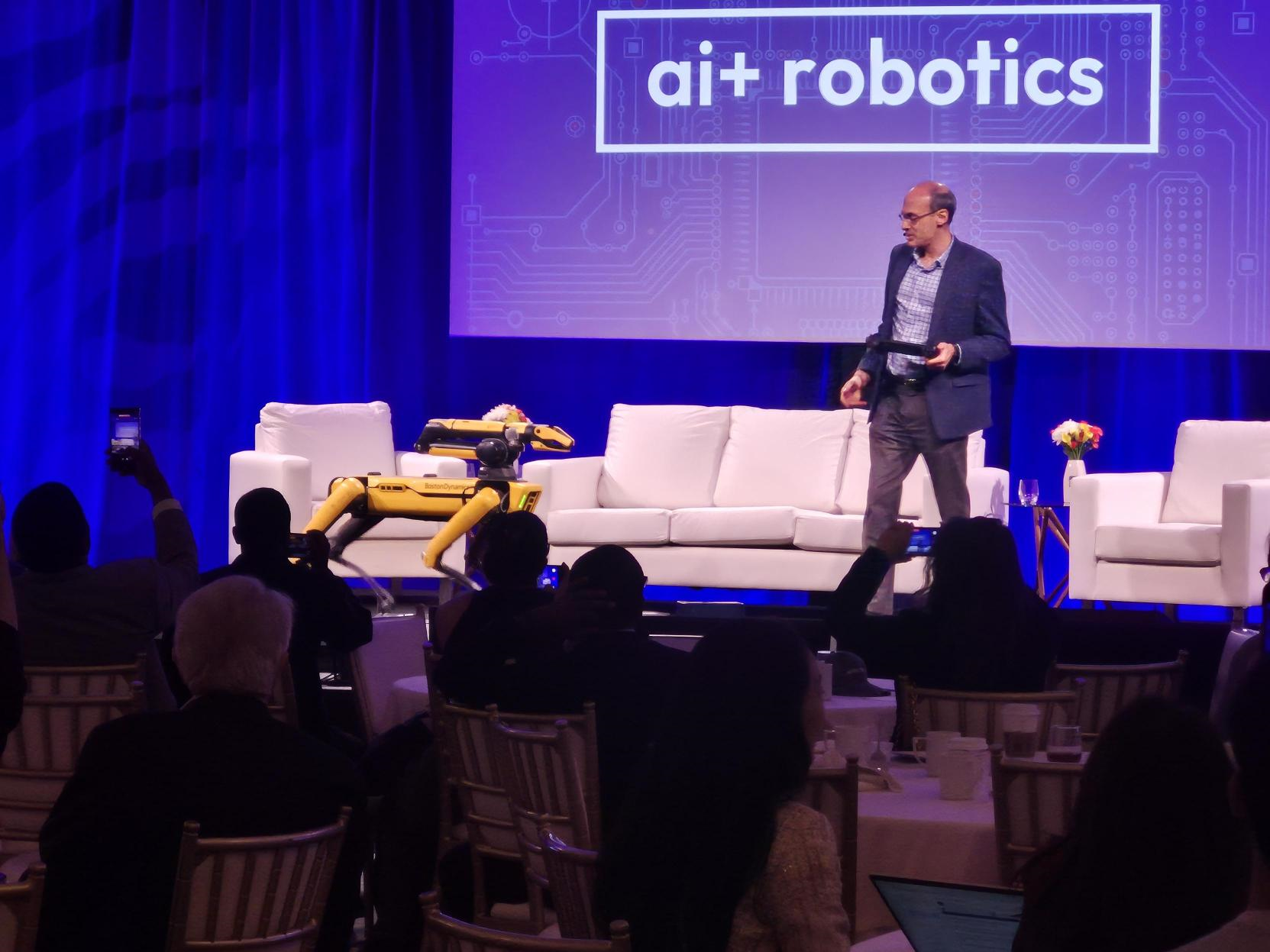 Boston Dynamics’ yellow Spot robot demonstrated onstage beside a presenter as conference attendees watch and take photos.