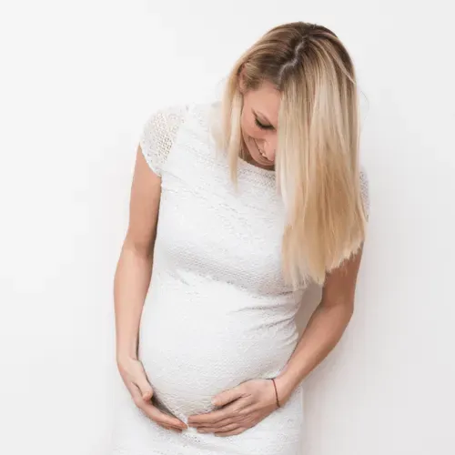 Femeie însărcinată în rochie albă ținându-se de burtă | Lumipeek