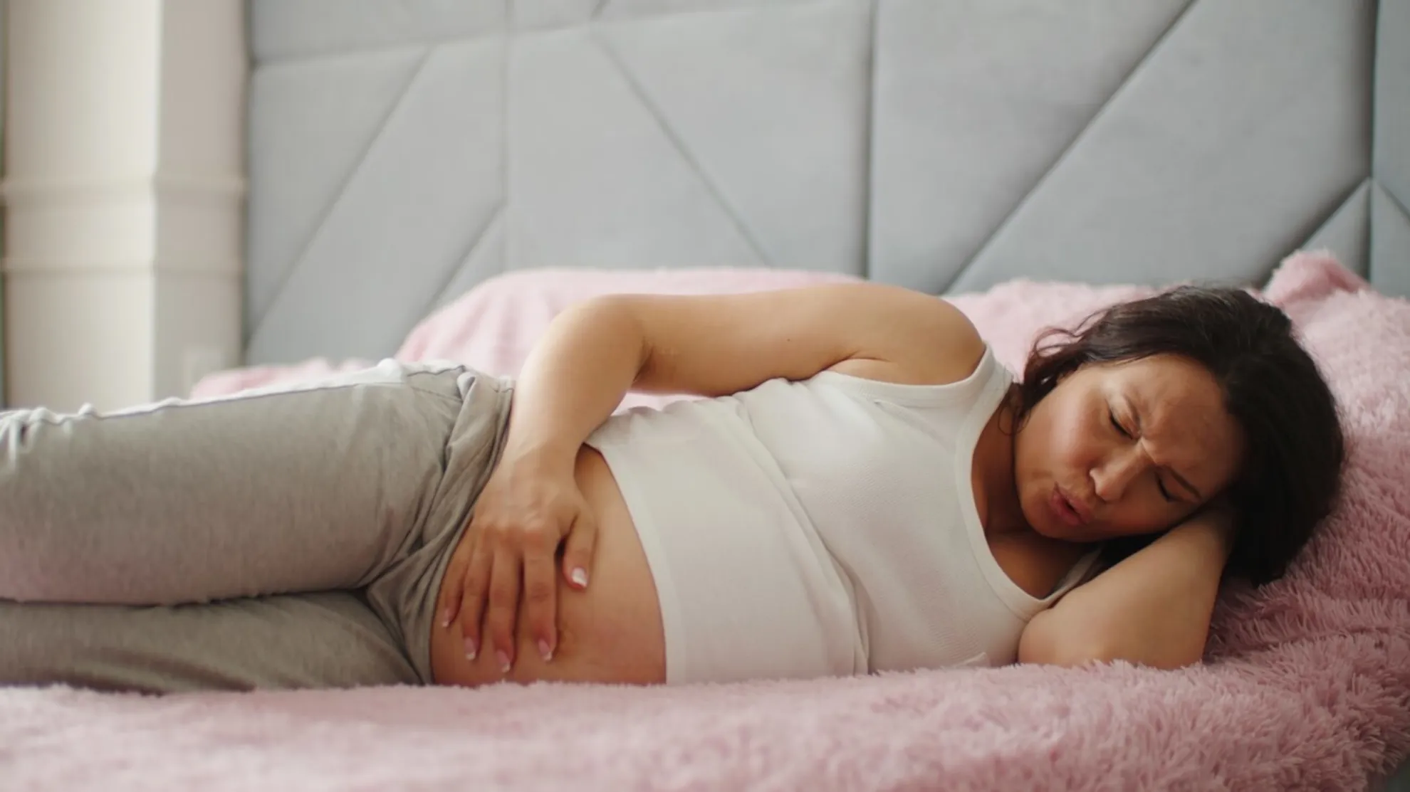 femeie însărcinată stând întinsă în pat ținându-se de burtă | durere înțepătoare de burtă în sarcină