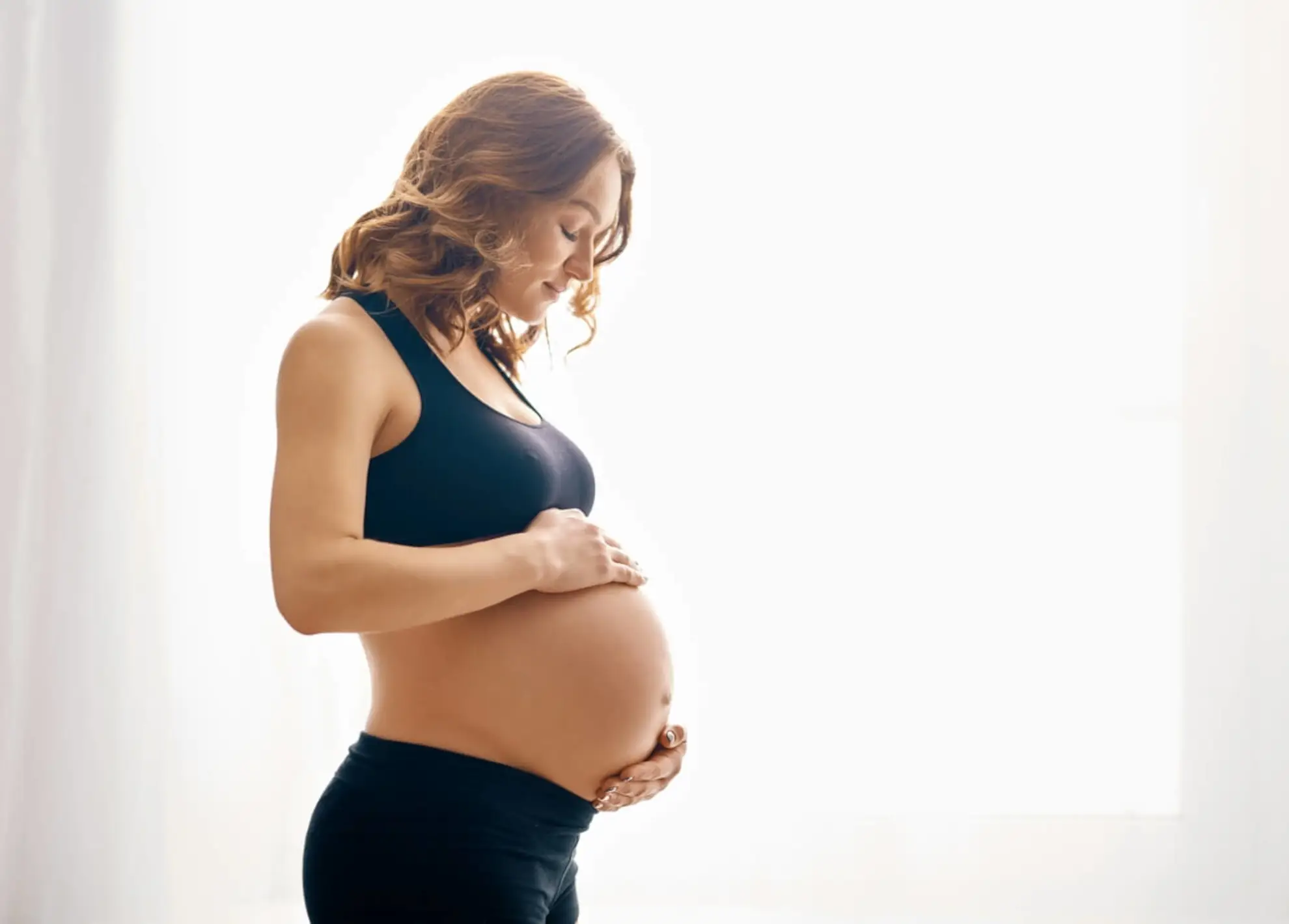 femeie însărcinată stă la fereastră ținându-se de burtă | biopsia de vilozități coriale