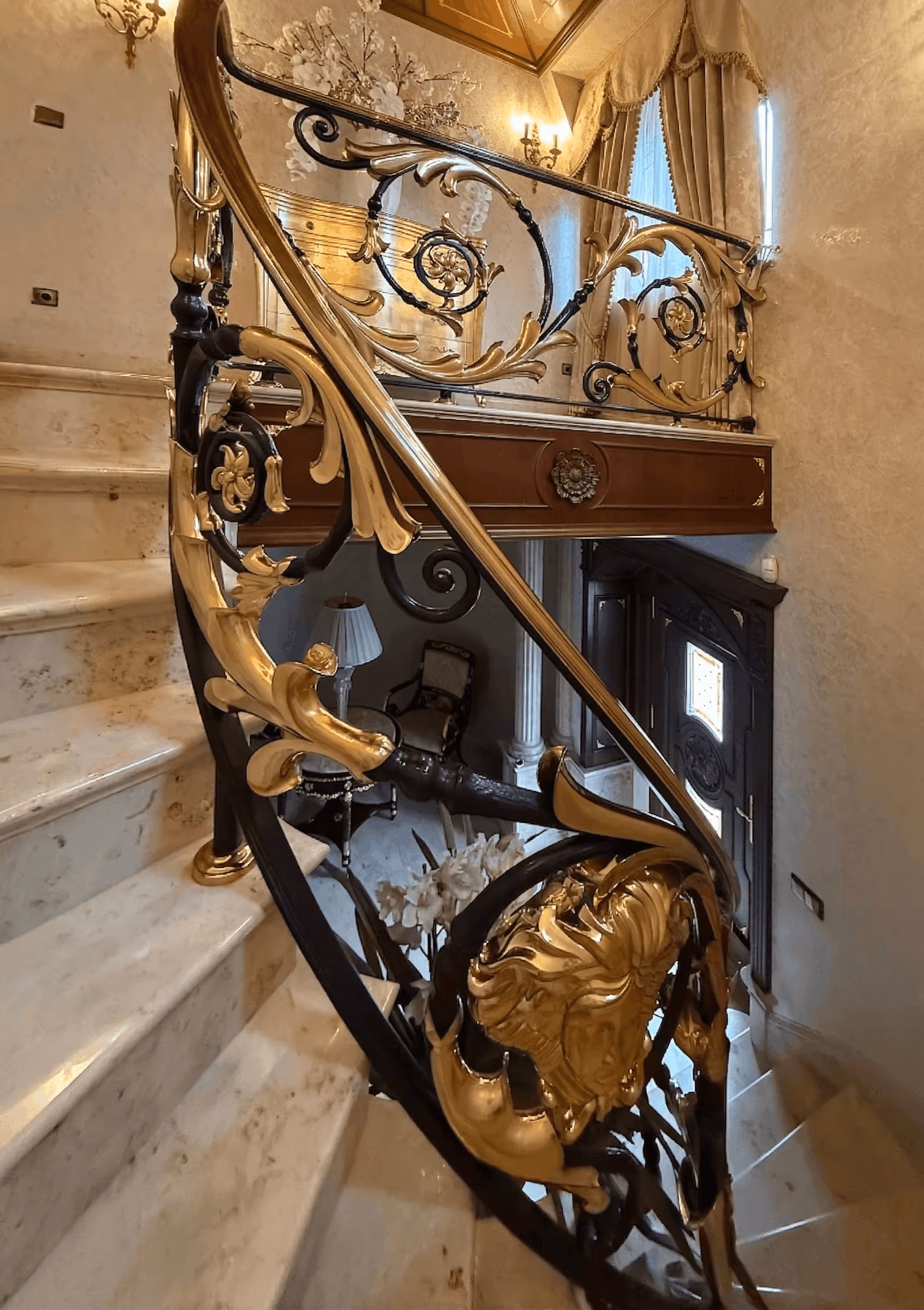 Marble spiral staircase with ornate black and gold wrought iron railing and elegant interior decor.