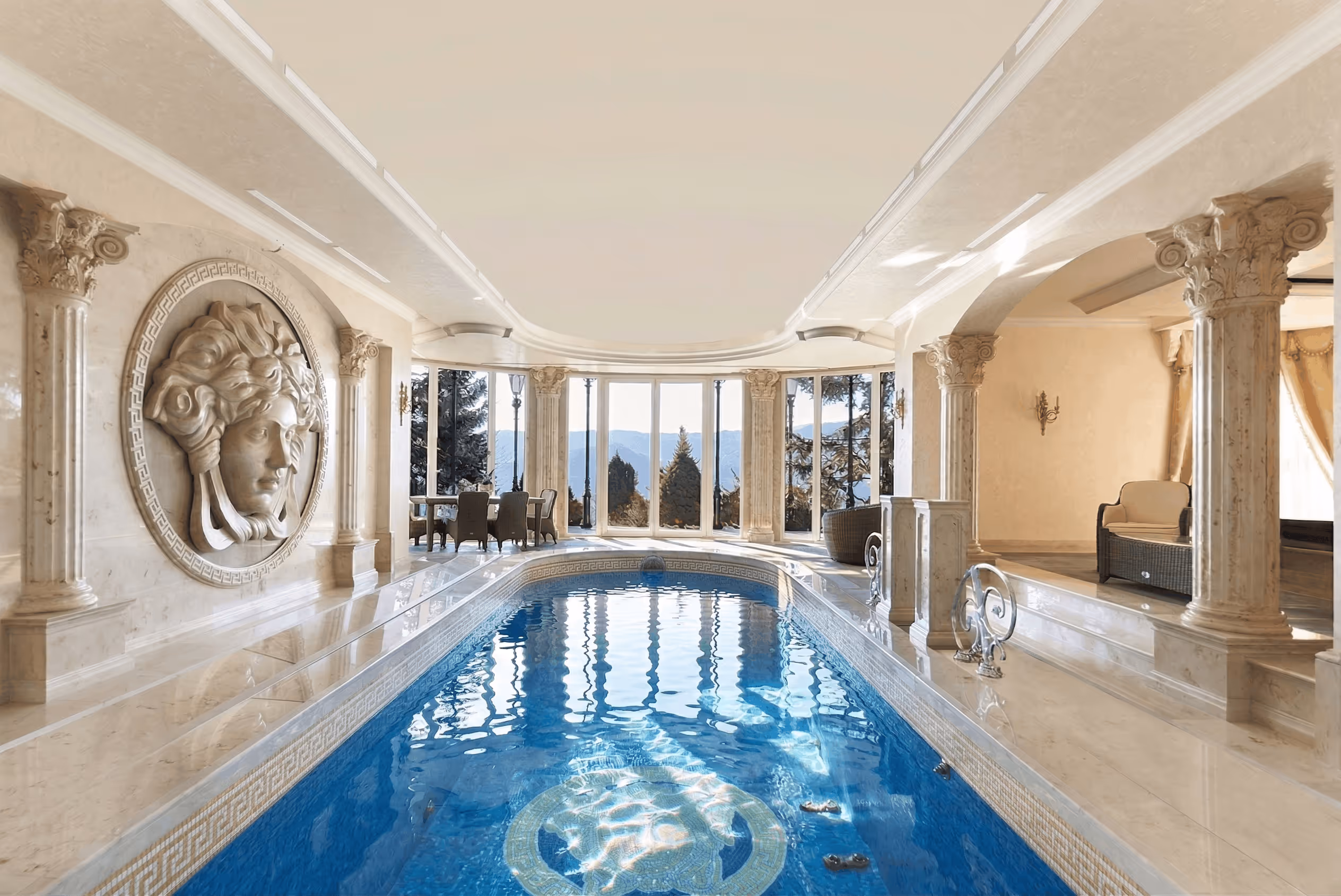 Indoor pool with blue water, marble columns, wall sculpture, and large windows showing mountain views.
