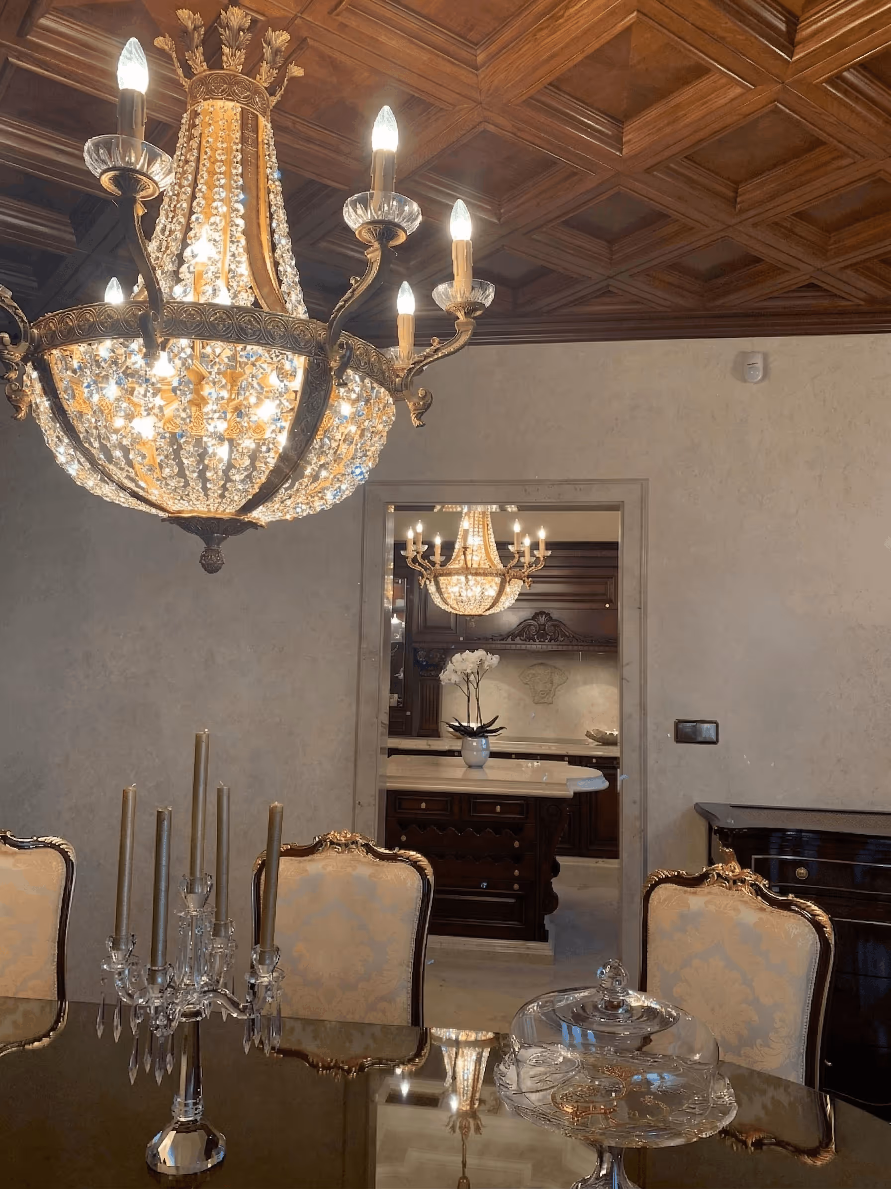 Elegant dining room with crystal chandelier, ornate chairs, and dark wood ceiling and furniture.