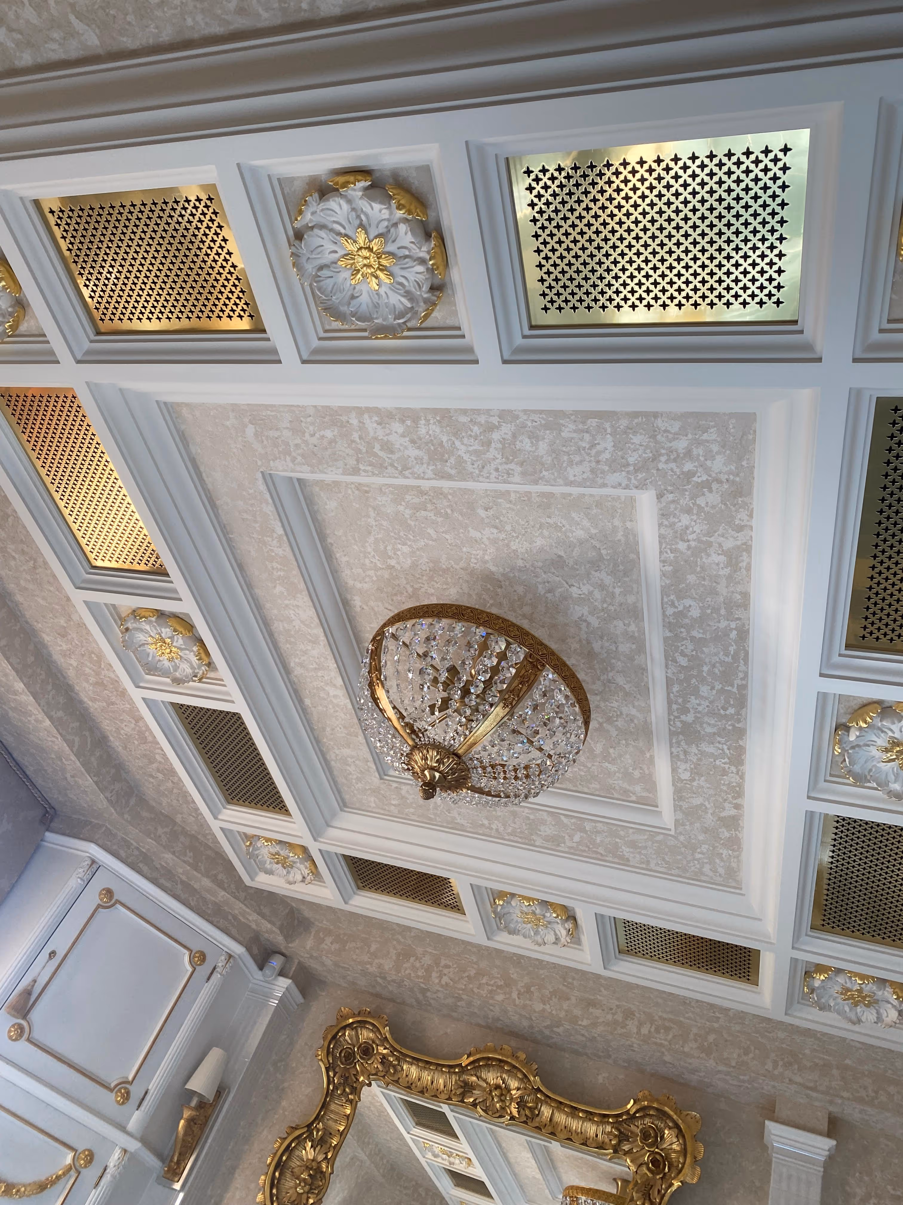 Ornate ceiling with gold and white decorative panels and a crystal chandelier in an elegant room.