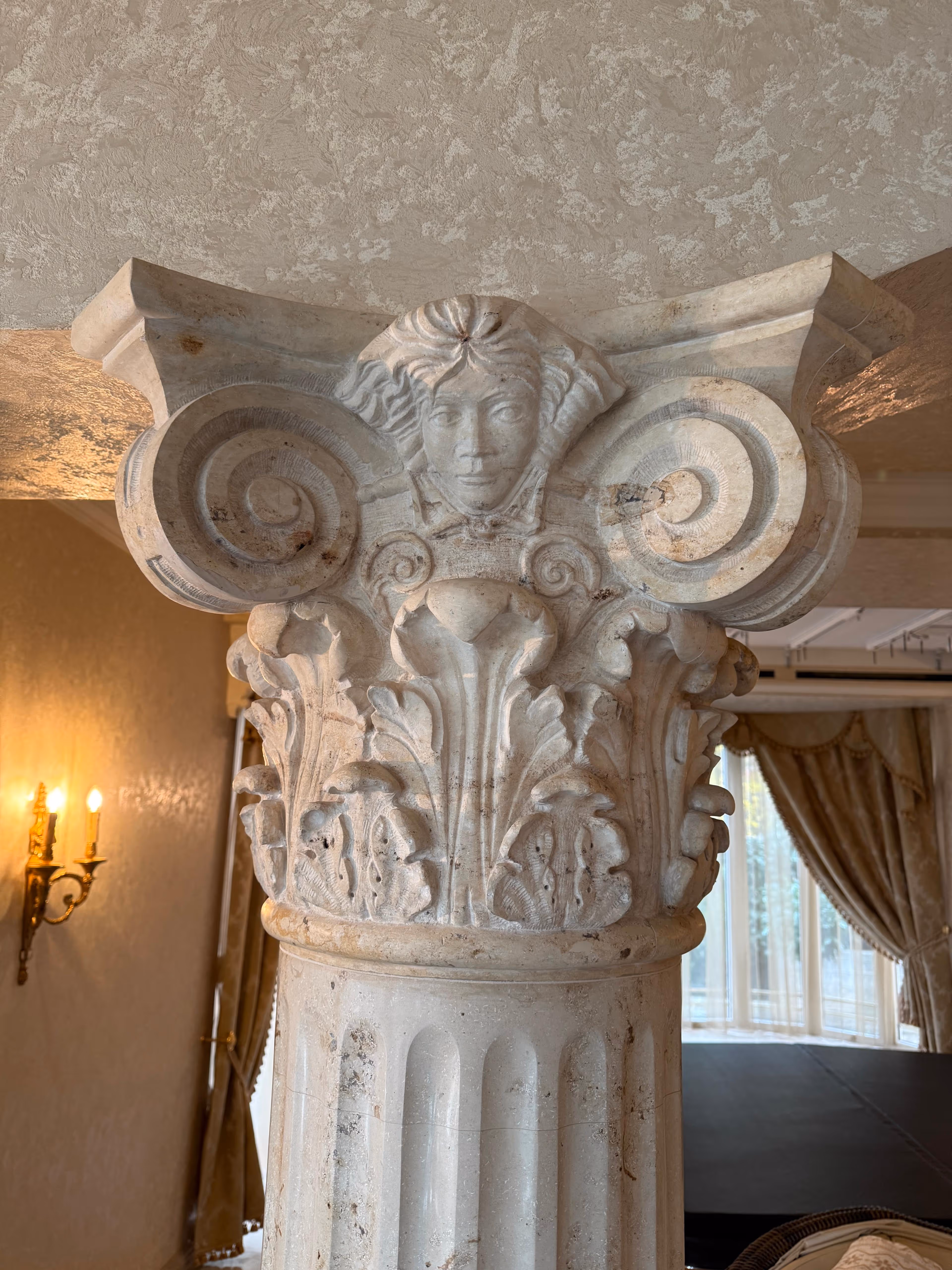 Carved stone column capital with a woman's face and decorative floral and scroll motifs indoors.