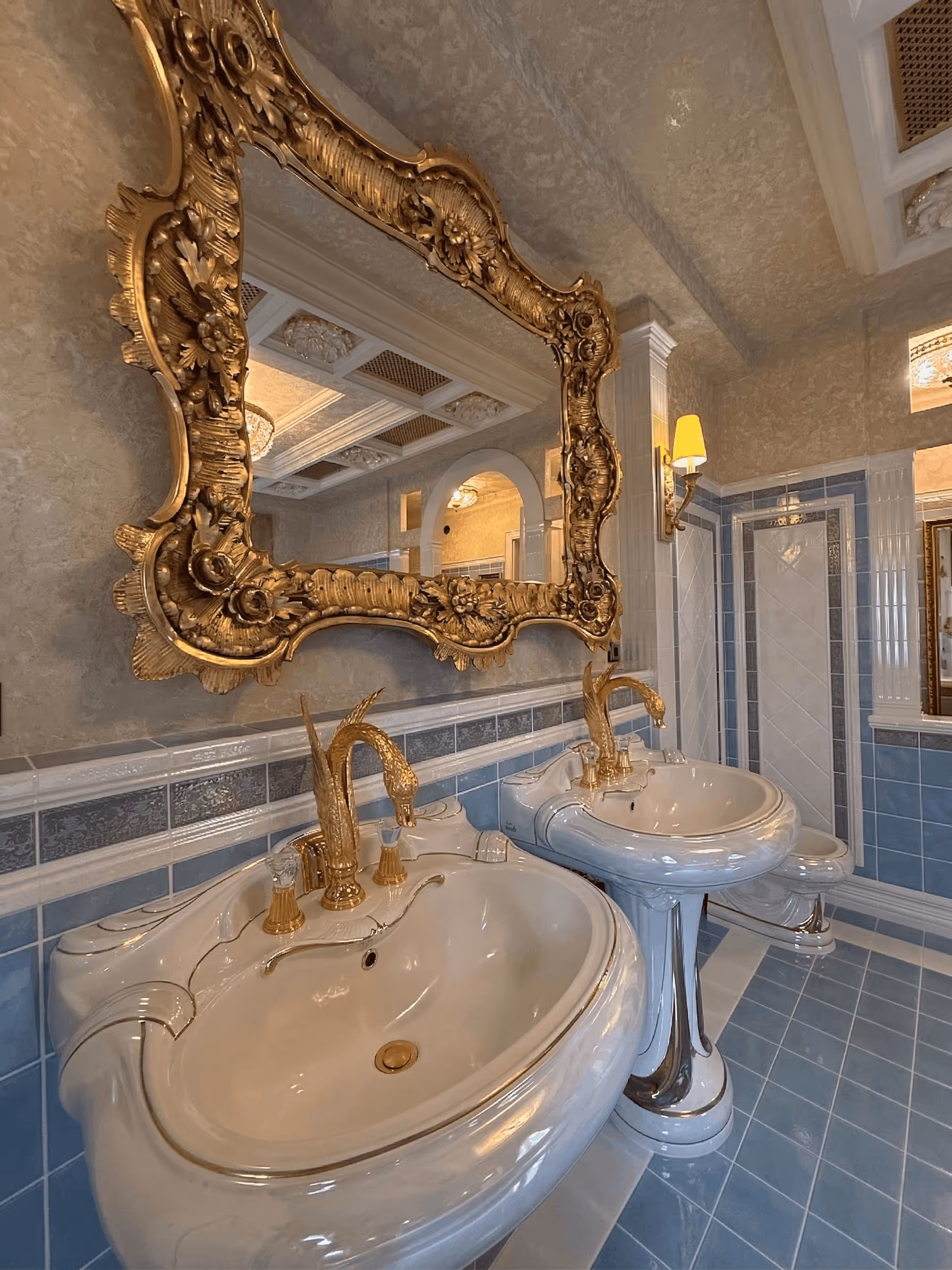 Bathroom with two ornate white sinks and gold swan-shaped faucets under a large gold-framed mirror.