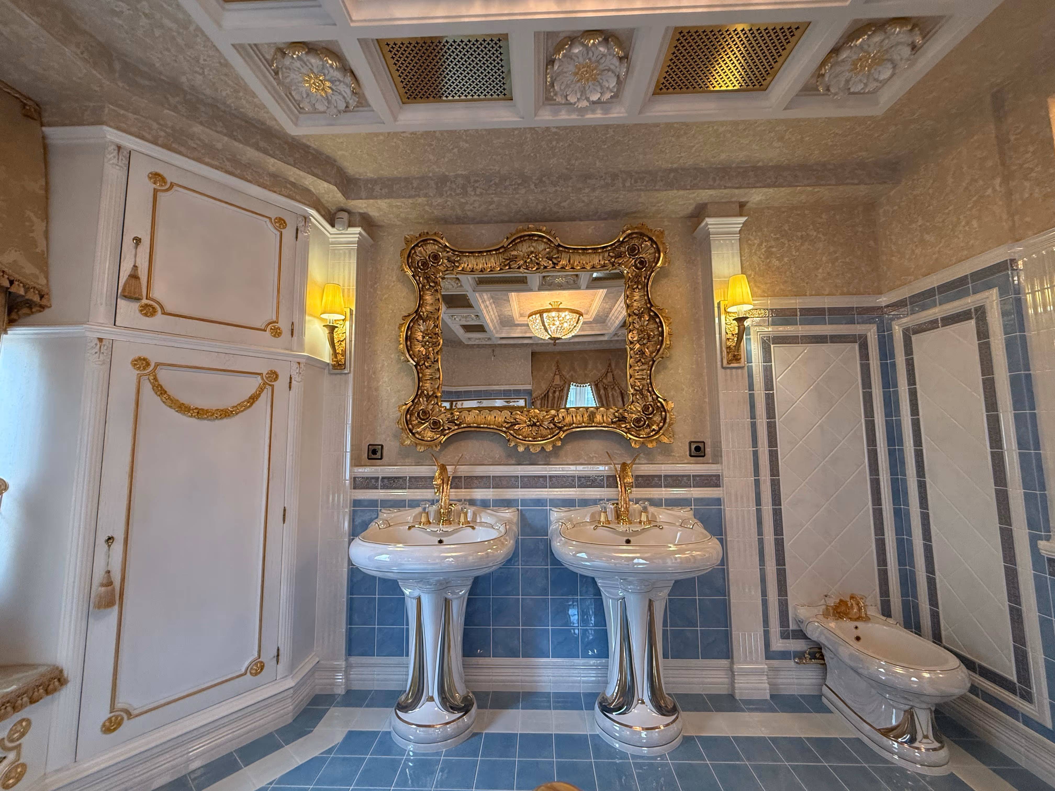 Elegant bathroom with two white pedestal sinks, gold-framed mirror, and blue tile floor and walls.
