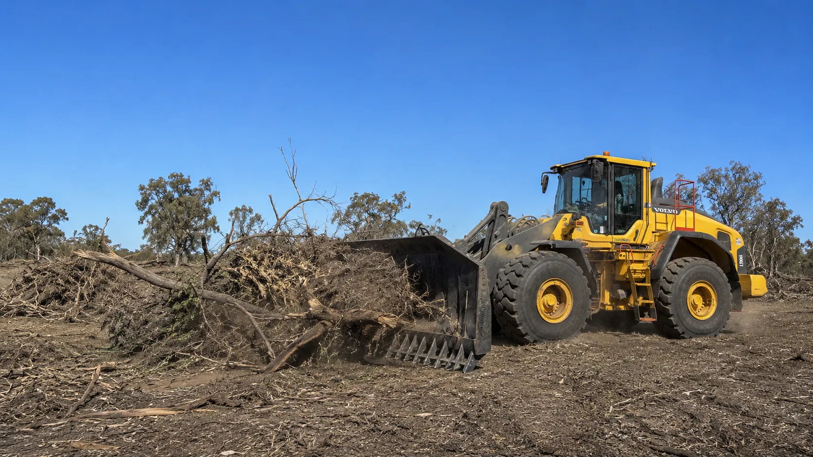 Volvo L150H stick raking a scrub pile in rural Queensland.