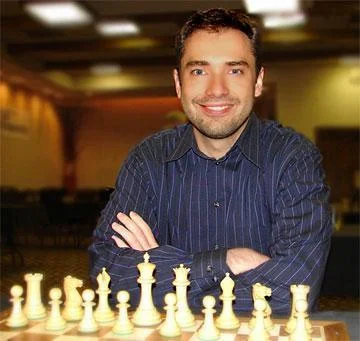 Photo of Eugene Perelshteyn sitting in front of a chess board, looking at the camera. 
