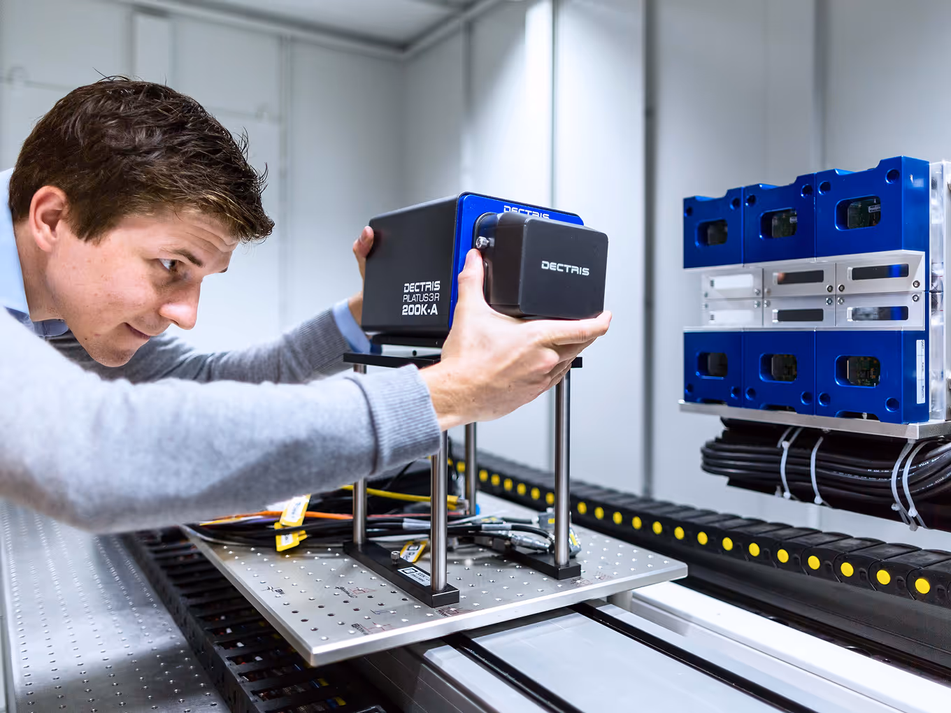 A man adjusts a Dectris detector labeled PLATU3R 200K-A mounted on a metal platform with electronic components in a lab setting.