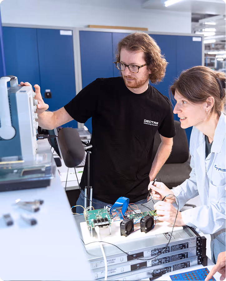 Two engineers working with electronic circuit boards and testing equipment in a lab environment.